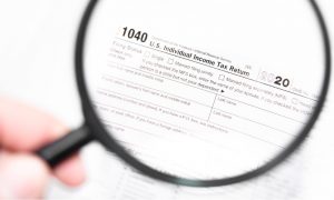 A person holding a magnifying glass over tax form 1040 to verify proof of income