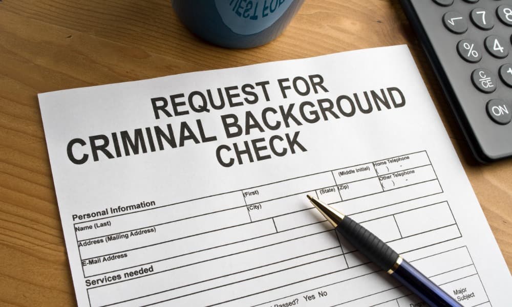 A criminal background check form sits with a pen on a wooden surface, ready for the rental applicant to fill out.